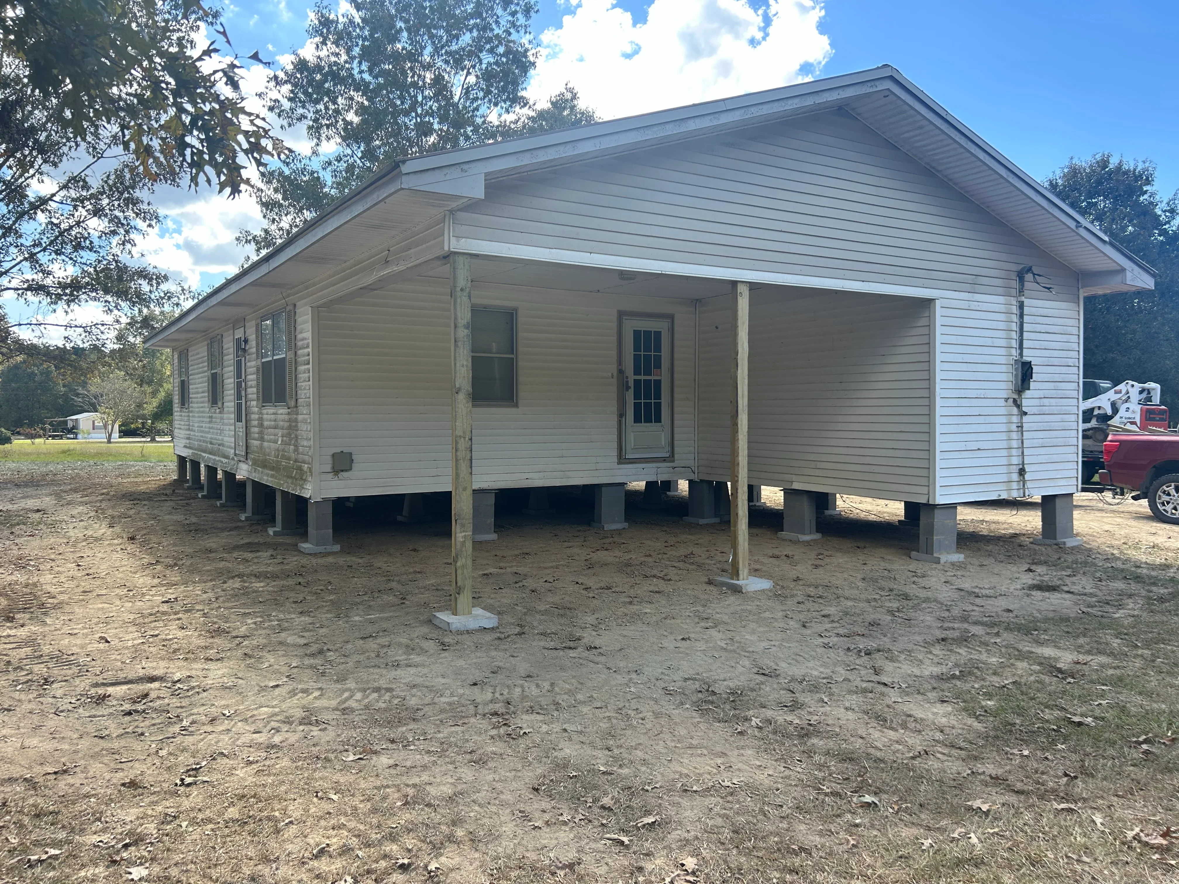 White mobile home elevated on new concrete piers and wooden support posts after releveling