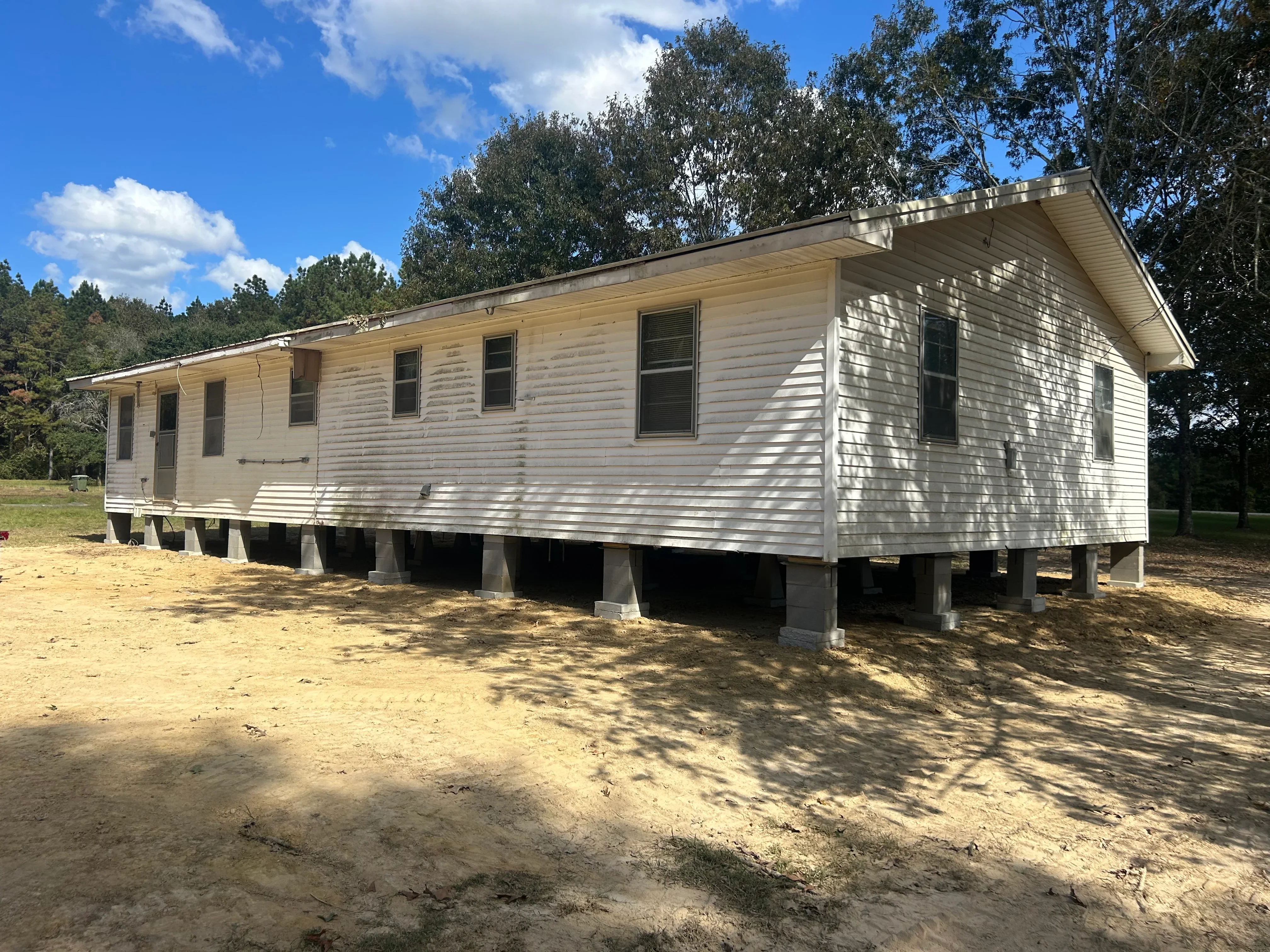 Mobile home elevated on new concrete block foundation piers with white vinyl siding