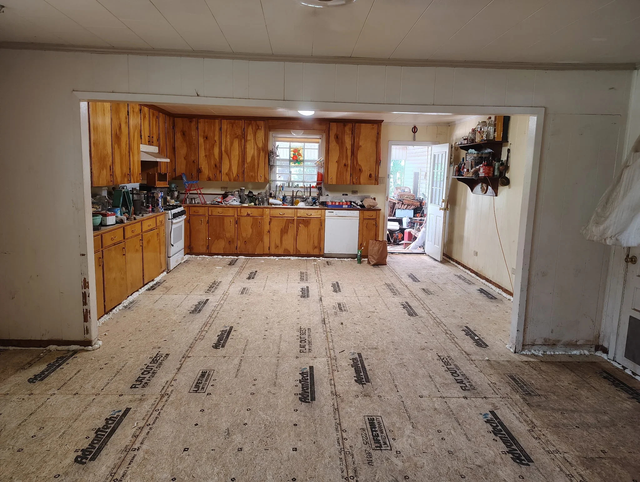 Kitchen with wooden cabinets and exposed subfloor underlayment during foundation leveling project