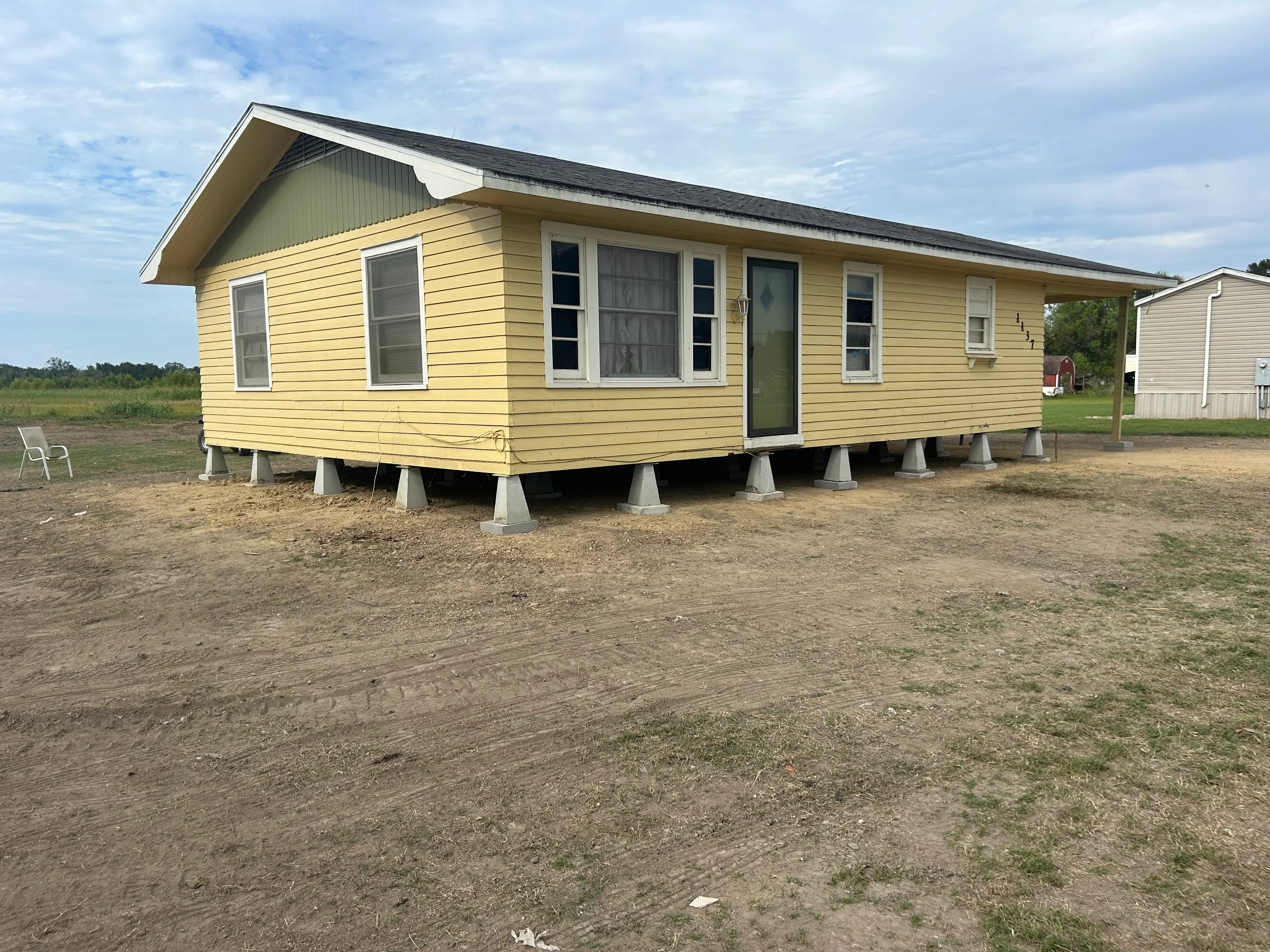 Yellow mobile home elevated on concrete pier foundation with vinyl siding and multiple windows