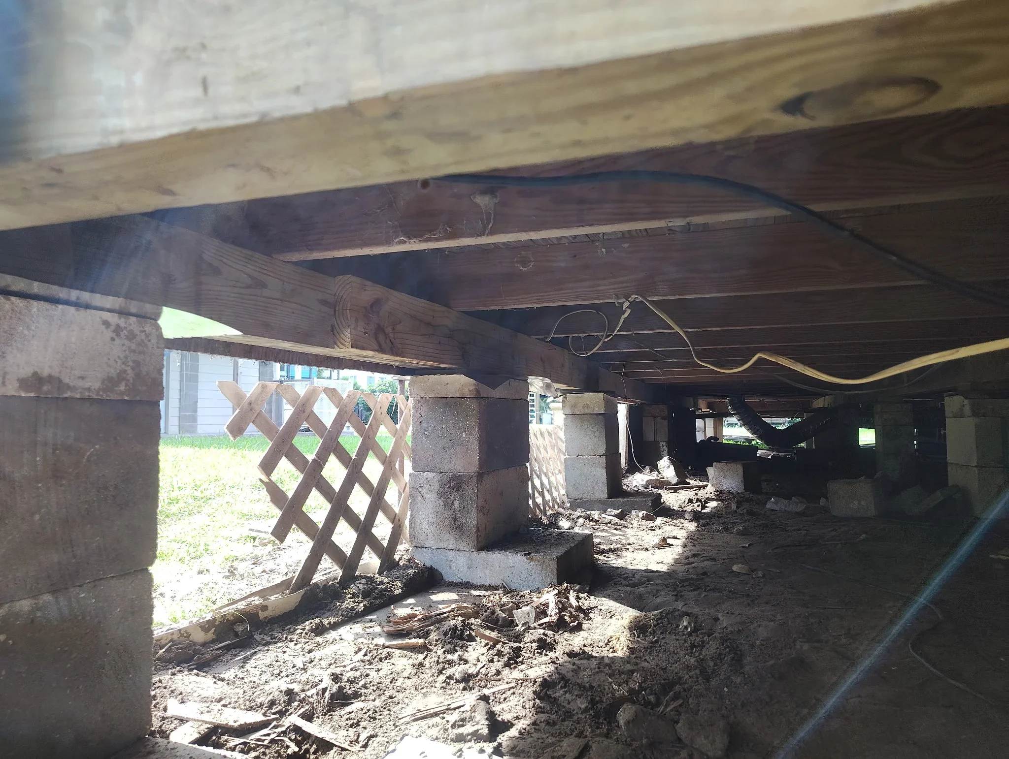 Concrete foundation piers and wooden support beams installed under a residential structure during foundation repair work