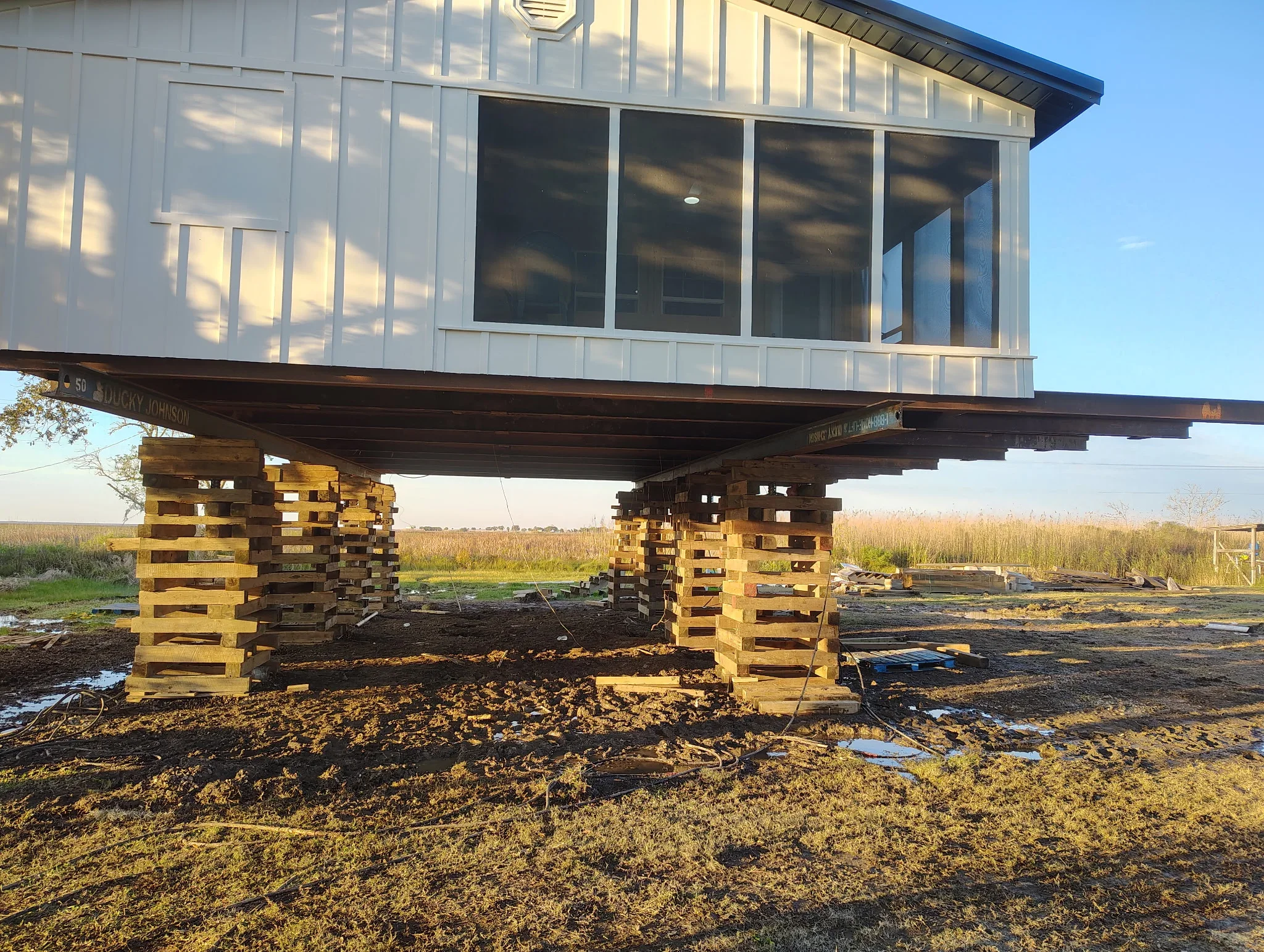 Wooden beam foundation supports stacked under elevated house with white siding