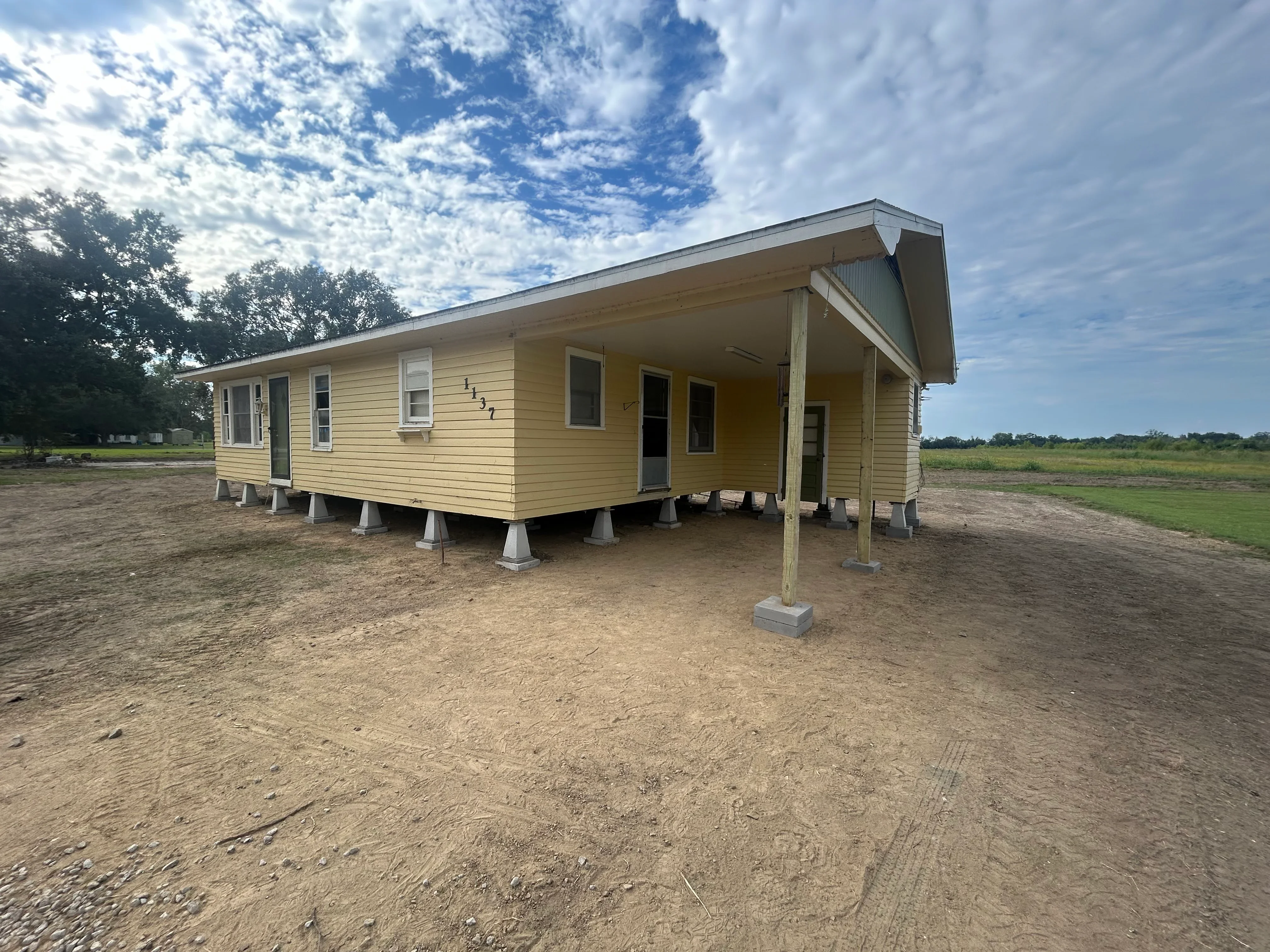 Cream-colored mobile home elevated on concrete piers with wooden support posts in rural setting