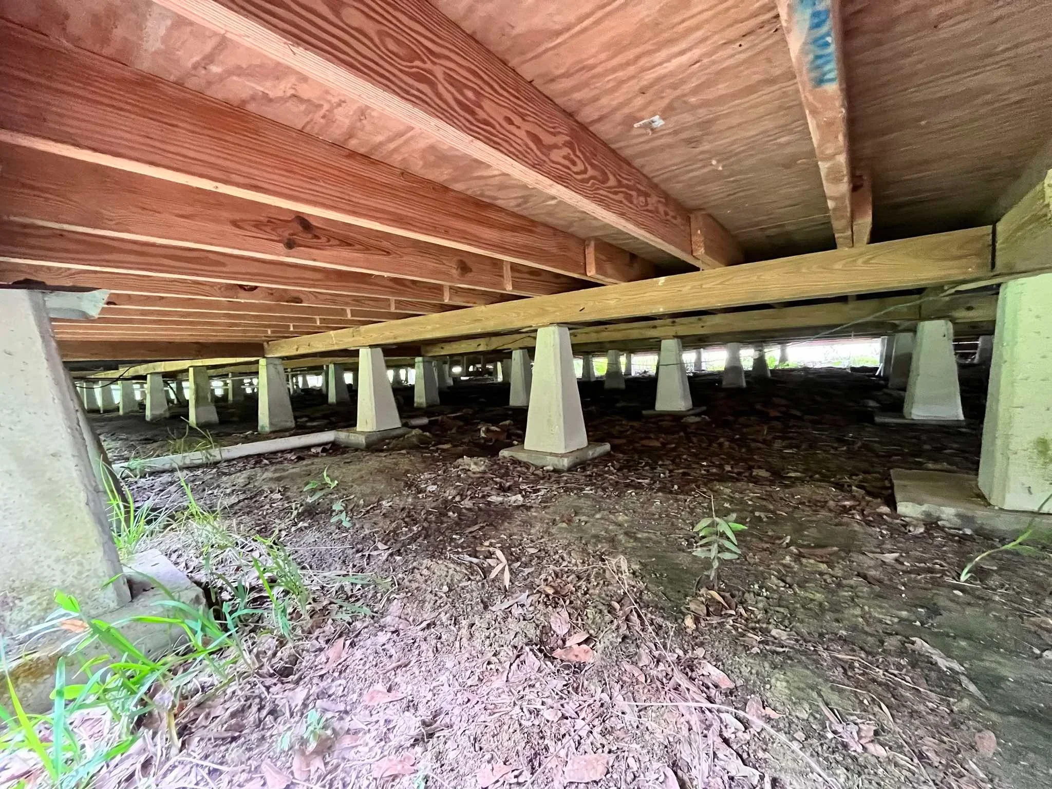 Crawl space with concrete support posts under wooden beam structure