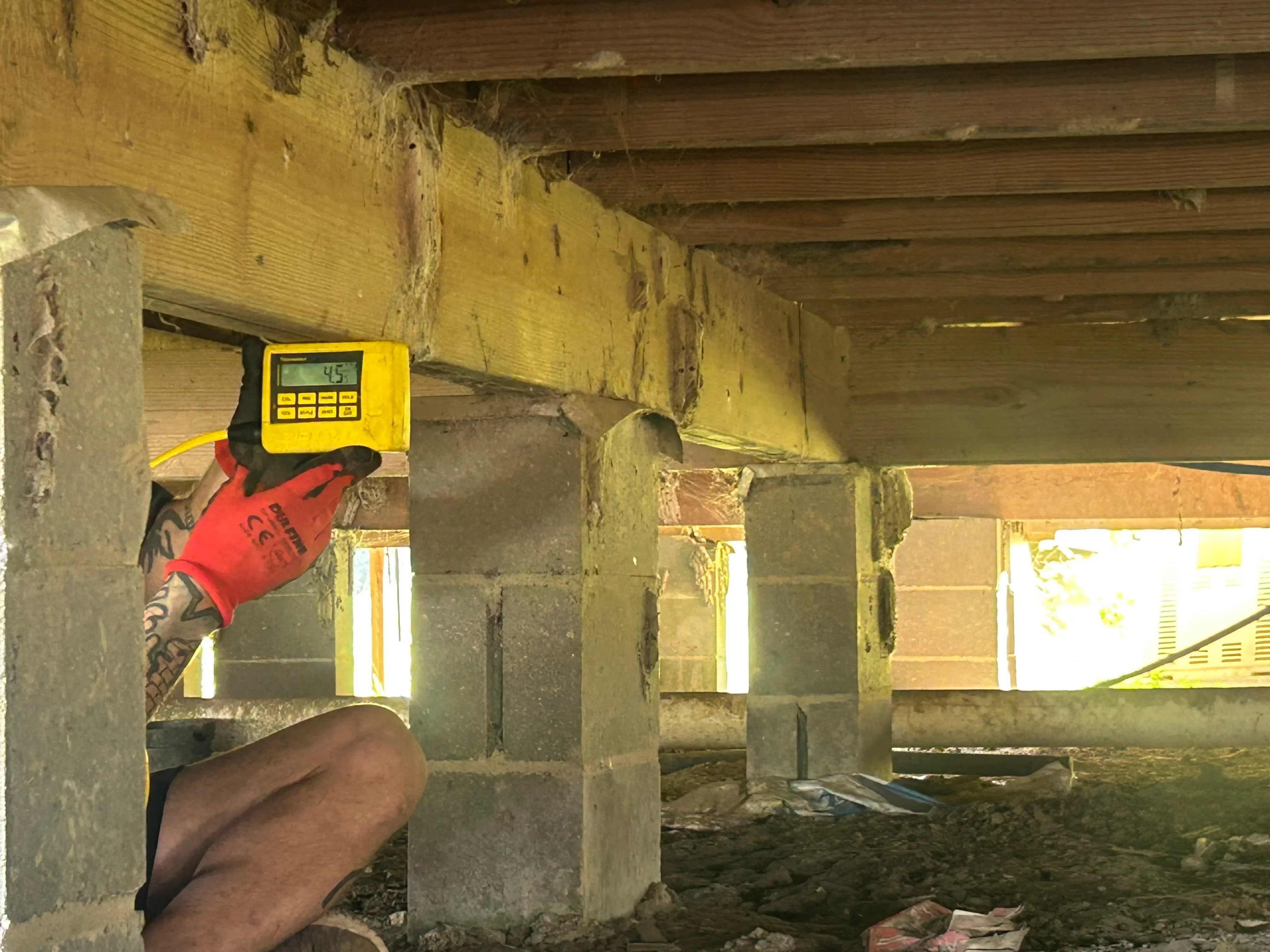 Foundation inspection in crawl space with laser measurement tool reading 45 degrees on wooden support beam