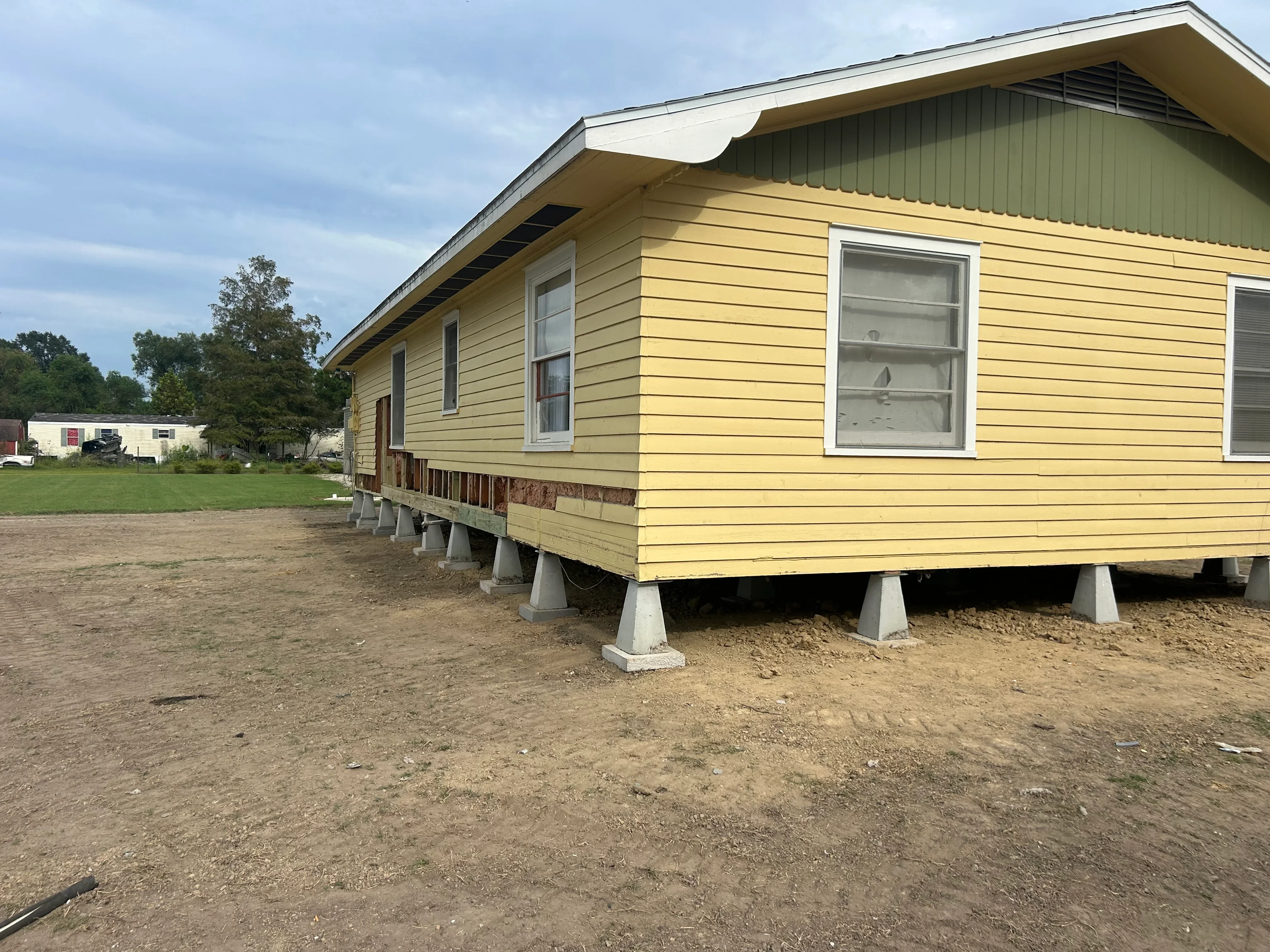 Yellow mobile home elevated on concrete pier supports for foundation leveling and repair