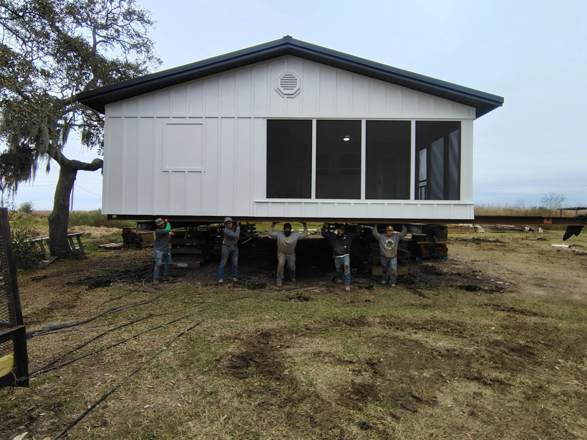 White mobile home elevated on foundation blocks with crew positioning structure during relocation